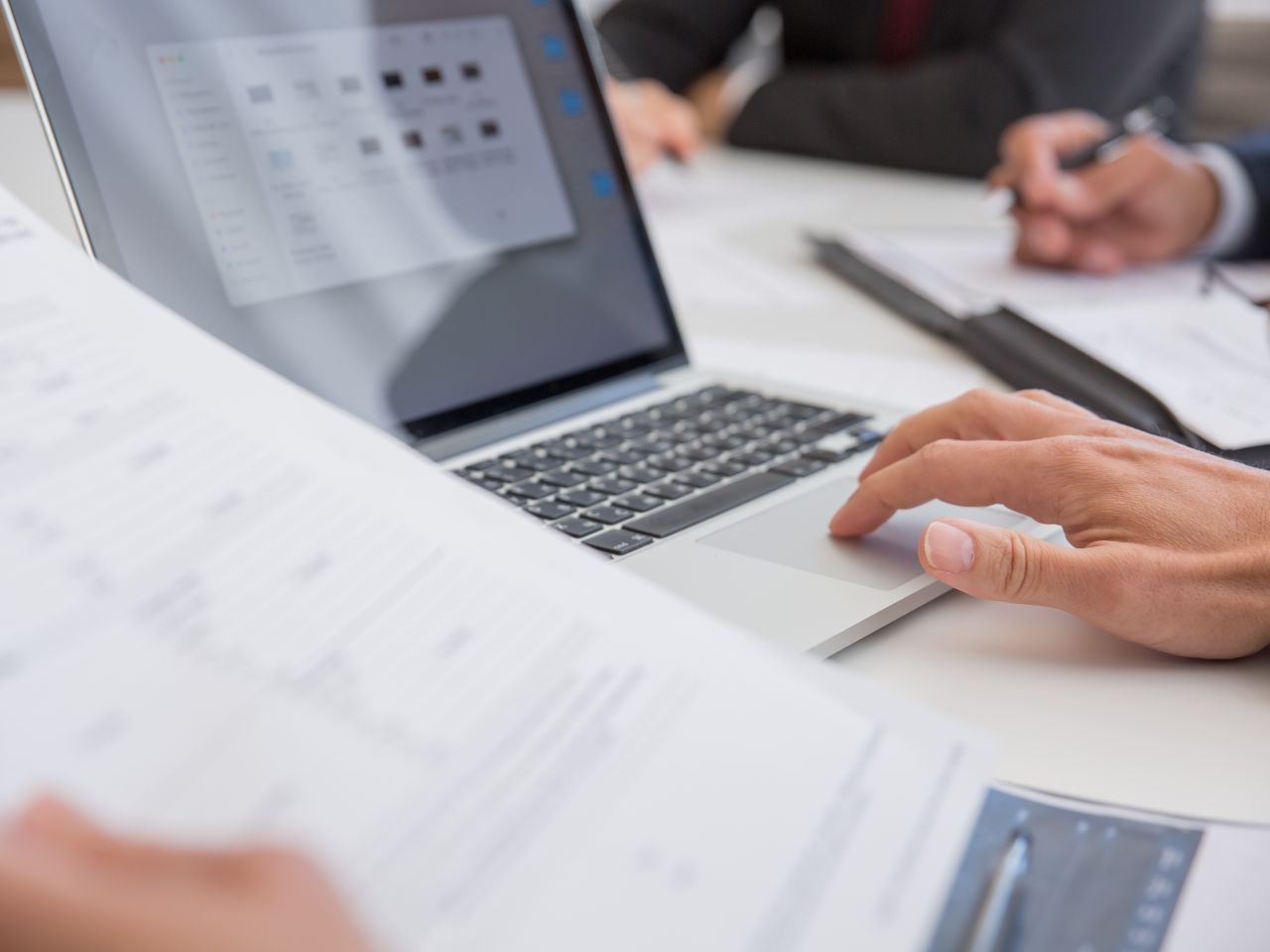 Professionals reviewing financial documents and analysis on an active laptop